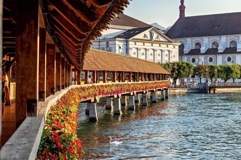 Historic wooden bridge decorated with flowers stretching across a river with old buildings in the