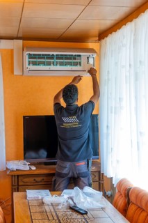 A man mounts an air conditioner over a television in the living room, air conditioning and