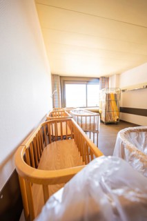 A room with several wooden cribs illuminated by daylight through a window, Obstetrics, Nagold,