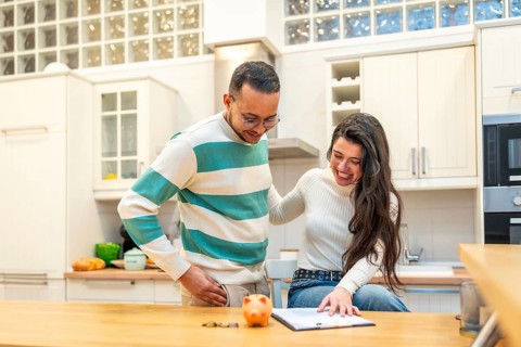 Young couple joyfully calculating savings, reviewing documents for financial planning and