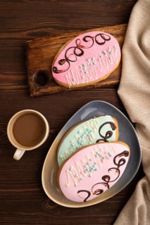 Glazed pink and blue decorated cookies, cup of coffee, on brown wooden background with linen