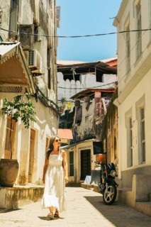 Woman tourist in white dress walks through beautiful Stone Town alley. Historic Zanzibar