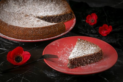 Sliced poppy seed cake on red plates with powdered sugar and poppies on a dark surface