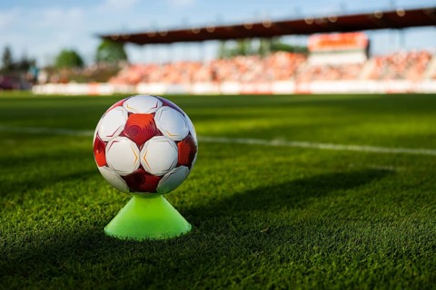 Soccer ball balanced on a training cone on a football pitch with stadium stands blurred in the