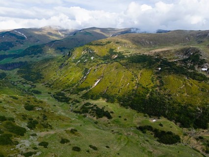 Green hills and mountains stretch under a cloudy sky in a quiet, expansive landscape, aerial view,
