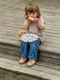 Little Caucasian girl, 3 years old, sitting on a wooden deck and eating a cake in Ystad, Skåne