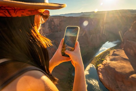 Woman photographing horseshoe bend and the colorado river from a cliff at golden hour in page,