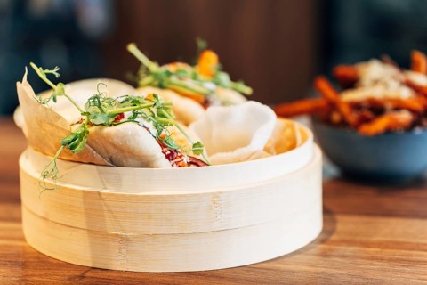 Freshly steamed bao buns in a traditional bamboo steamer, filled with vegetables, herbs, and sauce.