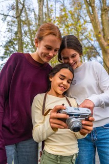 Three happy sisters looking at images on a vintage camera, sharing joy and bonding during a family