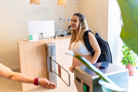 Pregnant woman smiling while passing through a turnstile at the gym entrance, getting ready for
