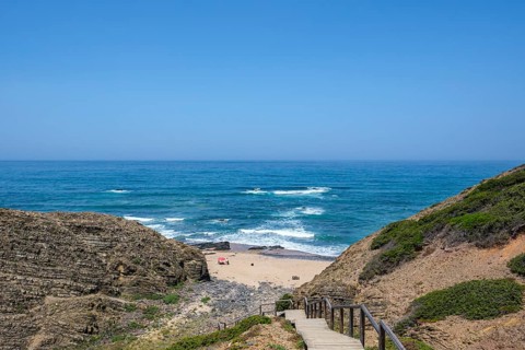 Wooden stairs lead down to a secluded beach surrounded by cliffs and the blue sea under clear
