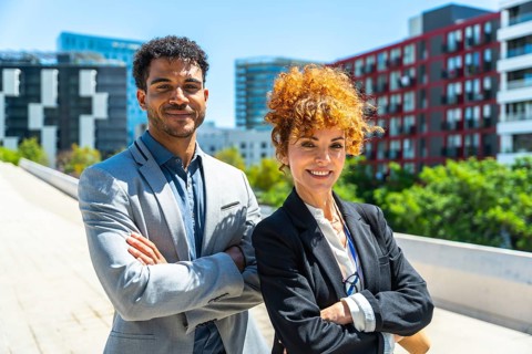 Diverse business partners smiling, standing outdoor with folded arms, expressing confidence,