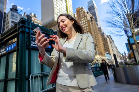 Young businesswoman smiling, navigating her modern smartphone device on a vibrant manhattan city