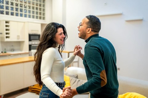 Happy diverse couple holding hands and dancing intimately in a modern open plan living room and