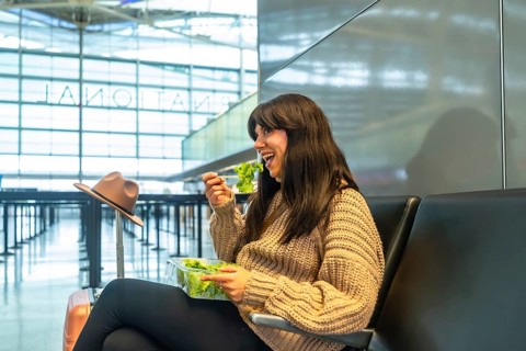 Young female traveler with dark hair sitting on a black bench in a modern airport terminal,