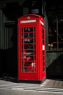 A classic red telephone box stands on a street in front of a restaurant, Royal Borough of