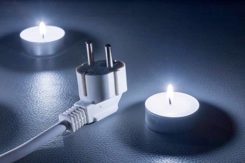 Two candles and an electric cable in cold light on a dark background, symbolic picture, power