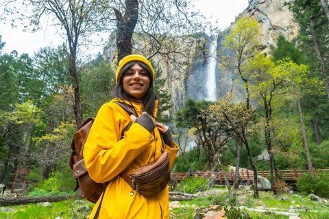 Woman in a yellow raincoat and hat smiling while exploring yosemite national park, enjoying the