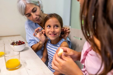 Happy grandmother is playing with her granddaughter. Placing cherry stems on her ears while another