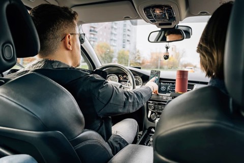 A man uses a navigator application in a mobile phone while driving and driving a car