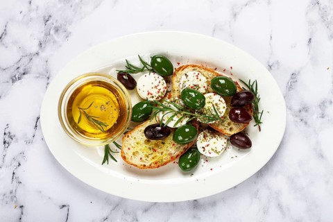 A plate with a snack, ciabatta bread with cheese and olives, olive oil, spices and herbs, top view,