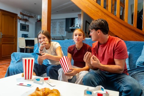 Family relaxing on a sofa watching tv together in a cozy living room, sharing popcorn and laughter