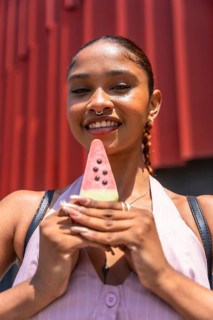 Young woman with a septum ring smiling and holding a refreshing watermelon shaped popsicle against