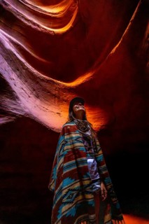 Woman standing inside antelope canyon wearing a colorful poncho, looking up at the sandstone walls