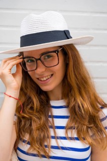 Young woman styling her hat, wearing glasses and a striped shirt, smiling at the camera with a