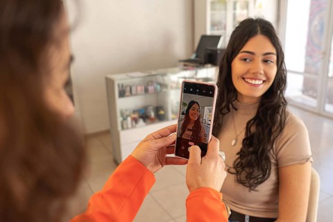 Professional makeup artist photographs a satisfied client with completed makeup using a smartphone