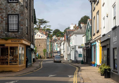 Traffic driving past shops in historic buildings in West Street, town of Ashburton, Devon, England,