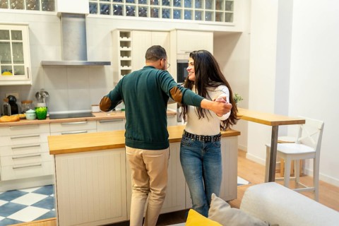 Cheerful couple holding hands while dancing playfully in a modern home kitchen, sharing a romantic