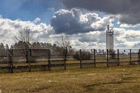 A meadow with a watchtower and a fence in the rain under dramatic cloudy skies, The Point Alpha