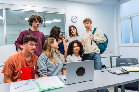 Diverse group of college students collaborating around a laptop in a bright classroom, studying