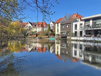 Row of houses on the riverbank with impressive reflection in water and clear blue sky,