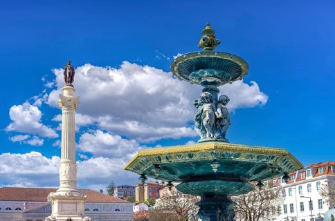 An ornate bronze baroque fountain near the monumental Column of Pedro IV under a vibrant blue sky