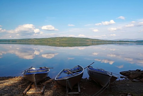 Three calm boats on the shore of a mirror-like lake under a blue sky, Störlien, Jämtland, Sweden