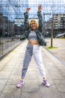 Carefree young woman dancing with arms raised in the city center, enjoying urban music and