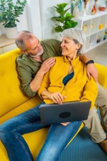 Vertical top view of a modern senior couple using laptop relaxed on the sofa together