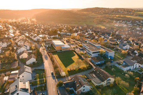 Suburban area with residential buildings and roads in hilly surroundings, sunset in the background,