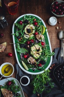 A vibrant salad featuring avocado, figs, cherries, and mixed greens on a rustic wooden table. The
