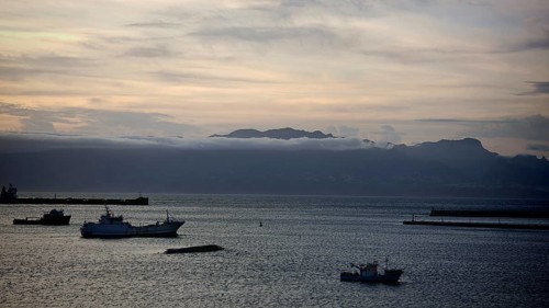 Boats on calm seas in front of a mountain range and cloudy sky at dusk, mountains of Santo Antao in