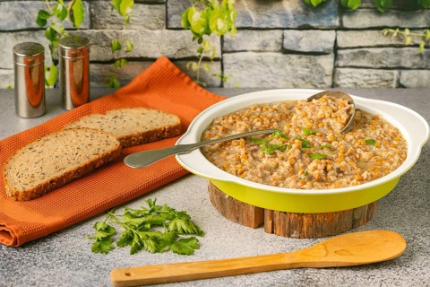 Lentils with bacon in a bowl with bread slices and ladle