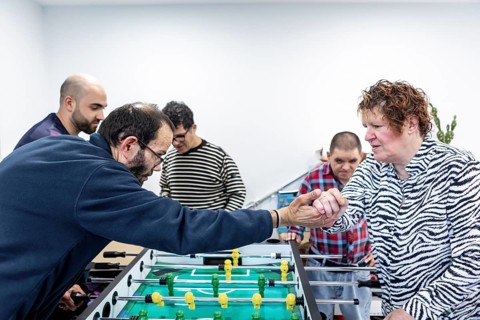 Residents of a mental health facility enthusiastically engage in a foosball game, showcasing