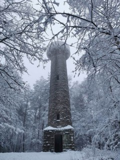 A tall stone tower rises amidst snow-covered trees and fog, Lucas Cranach Tower in Kronach,