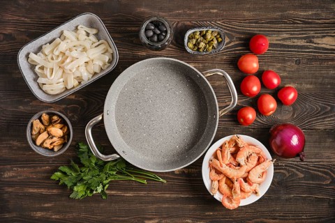 Fresh seafood ingredients are arranged on a wooden kitchen table. There are shrimp, mussels, squid,