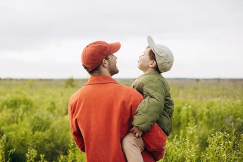 A father and his young son enjoy a serene walk through a lush green field, creating cherished