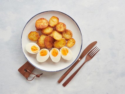 Crispy golden brown roasted potatoes sliced and hard boiled egg halves plate, knife and fork on the