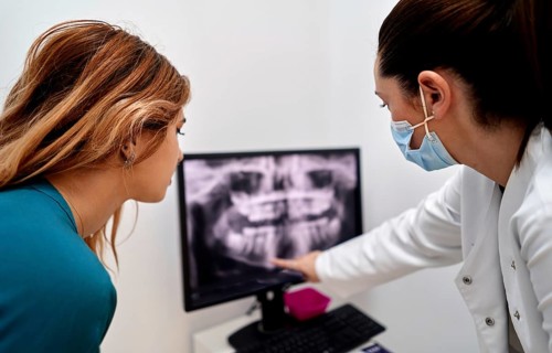A dentist in a dental clinic shows an x-ray on a computer screen to a patient, explaining details