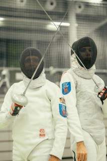 Two fencers hold their swords ready and look proudly at the camera as they pose in gear, fencing,